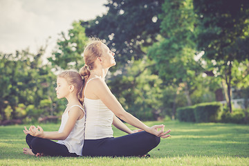 Image showing Mother and daughter doing yoga exercises on grass in the park.