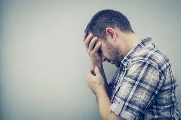 Image showing portrait one sad man standing near a wall and covers his face