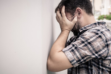 Image showing portrait one sad man standing near a wall and covers his face