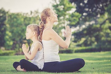 Image showing Mother and daughter doing yoga exercises on grass in the park.