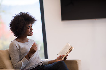 Image showing black woman reading book  in front of fireplace