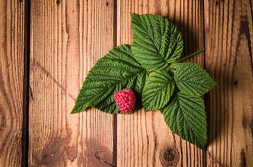 Image showing Berry raspberries with leaves on a wooden surface, close-up