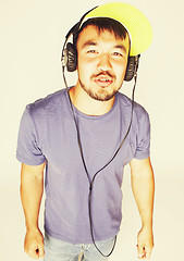 Image showing young asian man in hat and headphones listening music on white b