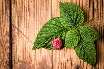 Image showing Berry raspberries with leaves on a wooden surface, close-up