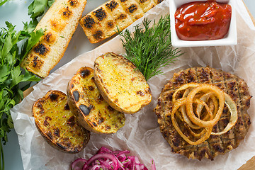 Image showing burger grill with vegetables, sauce on a wooden surface. potatoes and bread