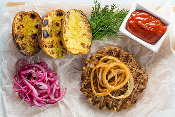 Image showing burger grill with vegetables, sauce on a wooden surface. potatoes and bread