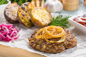 Image showing burger grill with vegetables, sauce on a wooden surface. potatoes and bread