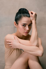 Image showing Tired ballet dancer sitting on the wooden floor on a pink background