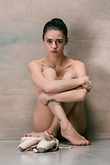 Image showing Tired ballet dancer sitting on the wooden floor on a pink background