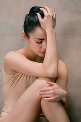 Image showing Tired ballet dancer sitting on the wooden floor on a pink background