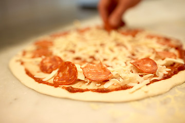 Image showing cook hands adding salami to pizza at pizzeria