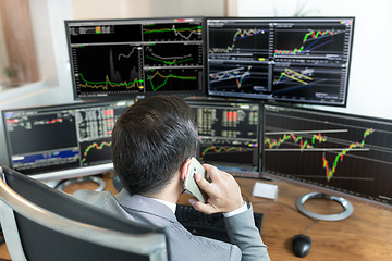 Image showing Over the shoulder view of stock broker trading online, talking on mobile phone.