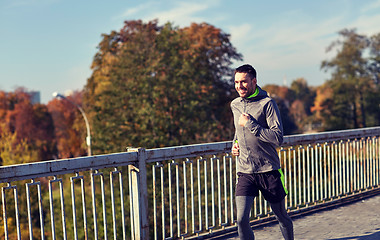 Image showing happy young man running over city bridge