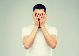 Image showing man in white t-shirt covering his face with hands