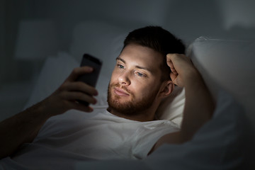 Image showing young man with smartphone in bed at night