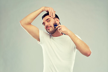 Image showing smiling man shaving beard with trimmer over gray