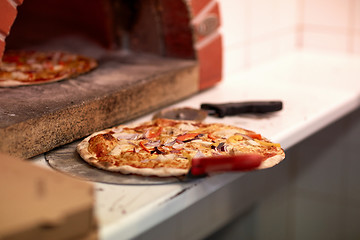 Image showing baked pizza on peel and oven at pizzeria