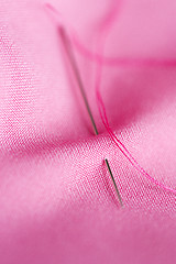 Image showing sewing needle with thread stuck into pink fabric