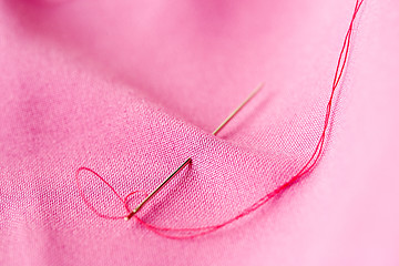 Image showing sewing needle with thread stuck into pink fabric