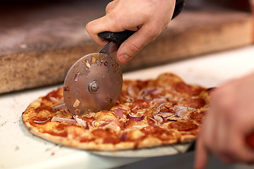 Image showing cook hands cutting pizza to pieces at pizzeria