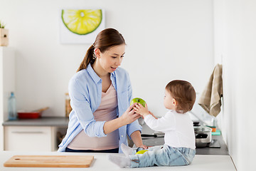 Image showing mother giving green apple to baby at home kitchen