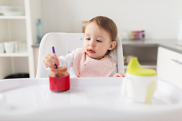 Image showing baby girl with spoon eating puree from jar at home