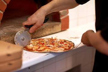 Image showing cook hands cutting pizza to pieces at pizzeria