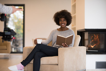 Image showing black woman reading book  in front of fireplace