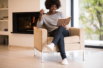 Image showing black woman reading book  in front of fireplace