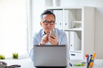 Image showing businessman with laptop texting on smartphone