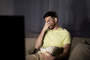 Image showing scared man watching tv and eating popcorn at night