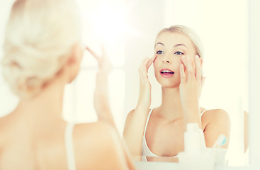 Image showing happy woman applying cream to face at bathroom