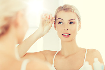 Image showing woman with tweezers tweezing eyebrow at bathroom