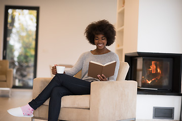 Image showing black woman reading book  in front of fireplace