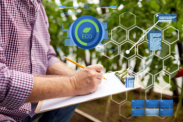 Image showing senior man writing to clipboard at farm greenhouse