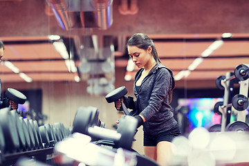Image showing young woman choosing dumbbells in gym