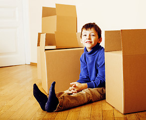 Image showing little cute boy in empty room, remoove to new house. home alone emong boxes close up kid smiling