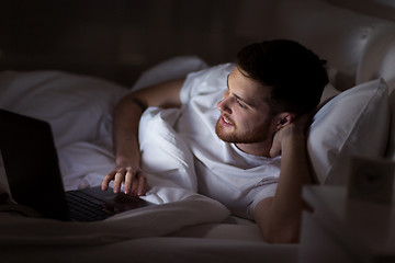 Image showing happy young man with laptop in bed at home