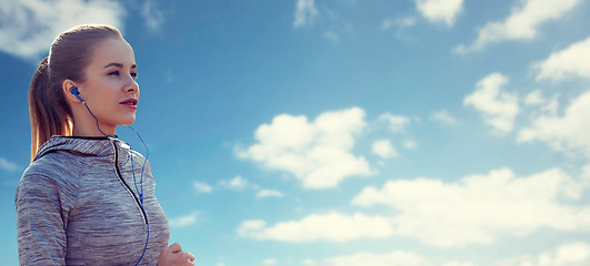 Image showing happy woman with earphones running over blue sky