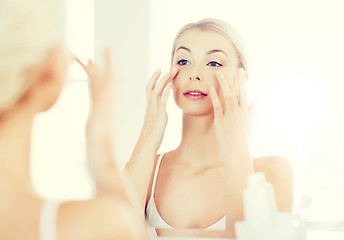 Image showing happy woman applying cream to face at bathroom