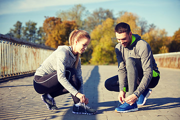 Image showing smiling couple tying shoelaces outdoors