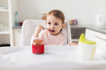 Image showing baby girl with spoon eating puree from jar at home