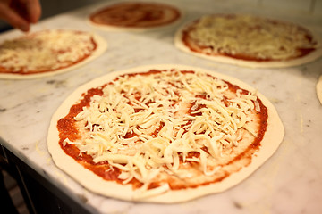 Image showing raw pizza with grated cheese on table at pizzeria