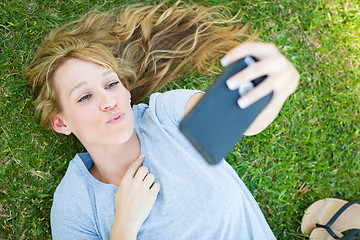 Image showing Young Adult Woman Laying in Grass Taking a Selfie with Her Smart