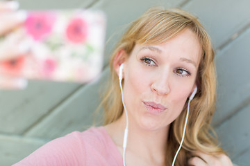 Image showing Young Adult Woman Wearing Earphones Taking a Selfie with Her Sma