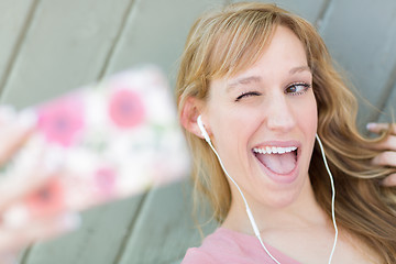 Image showing Young Adult Woman Wearing Earphones Taking a Selfie with Her Sma