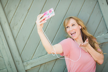 Image showing Young Adult Woman Wearing Earphones Taking a Selfie with Her Sma