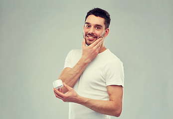 Image showing happy young man applying cream to face over gray