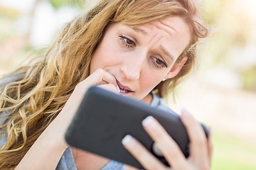 Image showing Concerned Young Woman Outdoors Looking At Her Smart Phone.