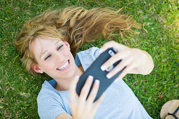 Image showing Young Adult Woman Laying in Grass Taking a Selfie with Her Smart